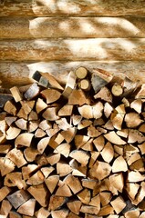 Stacked firewood near the wall of a log village house close-up. Firewood storage close up. Stocks of wooden logs close-up. Chopped wood and sun glare. Logging in the village. Woodpile with firewood 