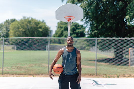 Athletic African-American standing on a basketball court with a ball under his arm