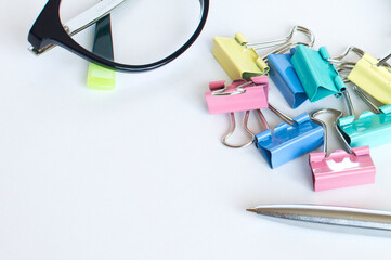 A pile of paper clips lies on a white background with a blue metal pen, and glasses