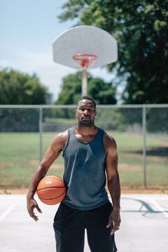 Athletic African-American standing on a basketball court with a ball under his arm