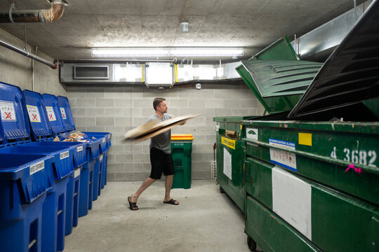 Man Throwing Cardboard Into Recycling Bin At Apartment