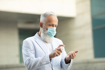 Coronavirus bearded senior man wearing face mask using antiseptic bottle dispenser hand sanitizer alcohol gel hand wash. Covid-19.
