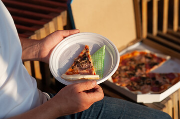 A man holds a slice of pizza in his hands. Fast food in the fresh air.