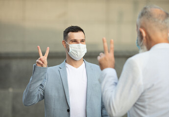 Two friends wearing face masks meeting and standing against the wall in outdoors for social distancing for infection risk and disease prevention COVID-19.