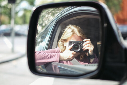 Photographer taking self portrait in car wing mirror