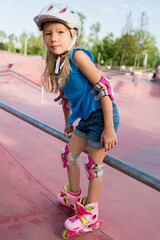 Cute girl learning to ride rollerblades on public park on sunny day. Children playing outside....