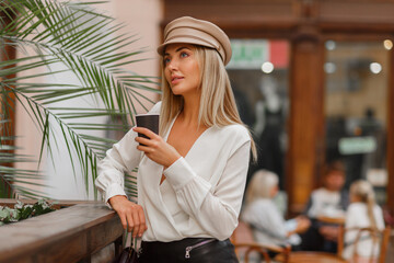 Fototapeta na wymiar Romantic pretty blond woman enjoying hot coffee outdoor. Wearing beige trendy beret. Autumn mood.
