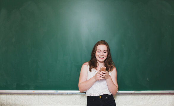 High school student standing in front of green chalkboard pretending to text on chalk brush