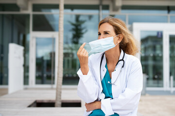 Ärztin im mittleren Alter vor einem Krankenhaus setzt einen Mundschutz auf