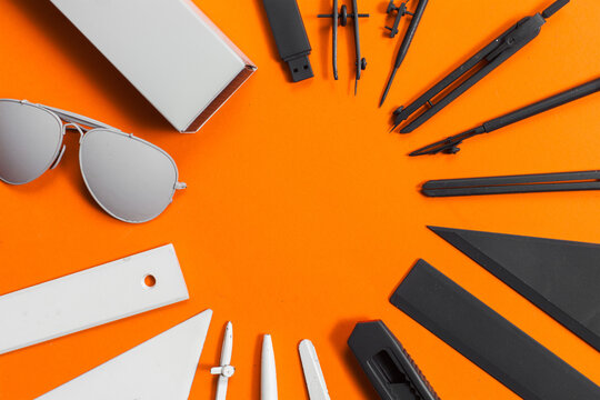 Office supplies in gradient from white to black color arranged in circle on orange background.
