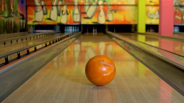 The bowling ball spins on the spot on the wooden floor of orange, slow-motion shooting.