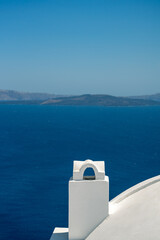 Fototapeta na wymiar White roof with chimney on the Caldera at Oia, Santorini island, Greece. beautiful blue seascape with volcano in the background
