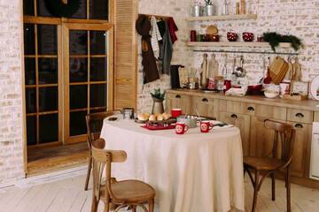 The kitchen is decorated with New Year's decor. Cookies are baked in the oven on the table in a red cup is cocoa.