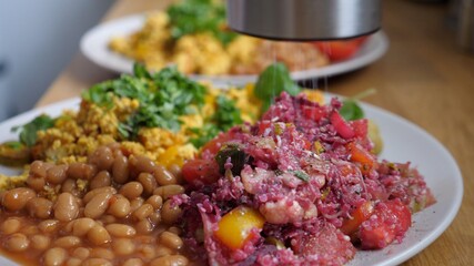 Close up of seasoning with grinder vegan breakfast of tofu omelet, beans and salad 