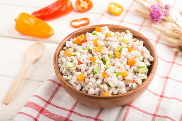 Pearl barley porridge with vegetables in wooden bowl on a white wooden background and linen textile. Side view, selective focus.
