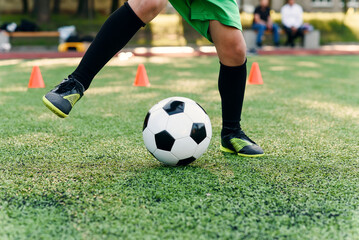 Obraz na płótnie Canvas Persistent teen soccer player kicking ball on field. Close up feet of footballer kicking ball on green grass.