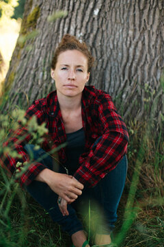 Young woman wearing plaid sitting by old oak tree, looking at camera