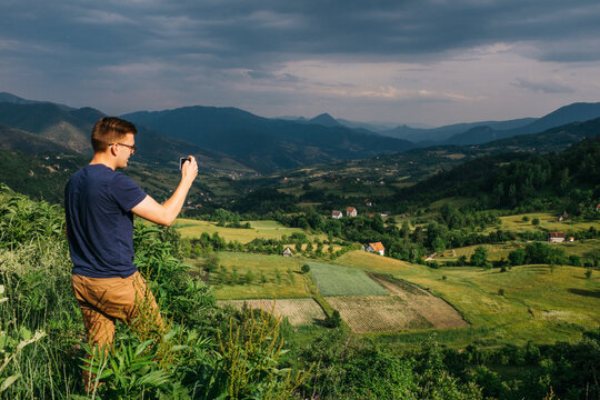 young man taking a picture in farm land valley nature