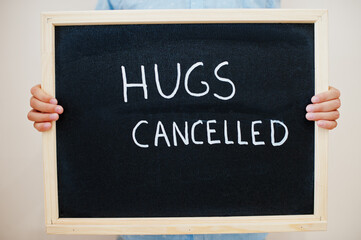 Hugs cancelled. Coronavirus concept. Boy hold inscription on the board.