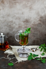 Tea with mint in a tall transparent glass on a ceramic stand. Hot warming aromatic drinks.