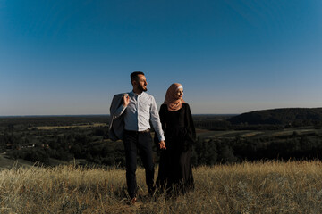 Muslim love story on the blue sky background. cheerful mixed couple smiles and hugs . Woman weared in hijab looks to her man. Advert for on-line dating agency