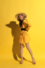 Pretty blonde girl with freckles in yellow outfit and straw hat on yellow background