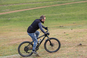 Obraz premium Sports brutal bearded guy on a modern mountain bike. Cyclist on the green hills in the spring.