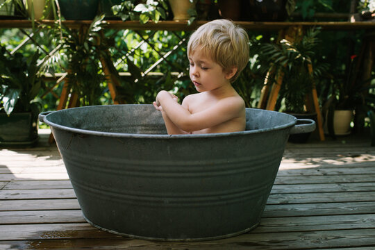 A child washes outside in an old-fashioned metal tub.