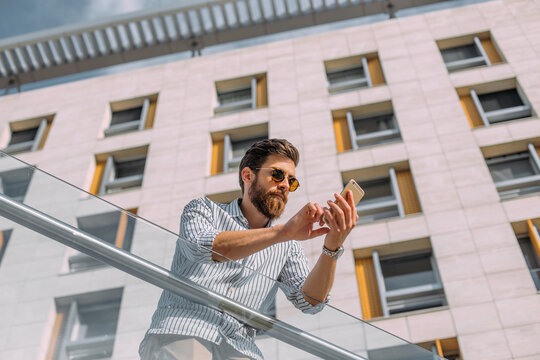 Young Caucasian businessman using phone in front of a corporate building.