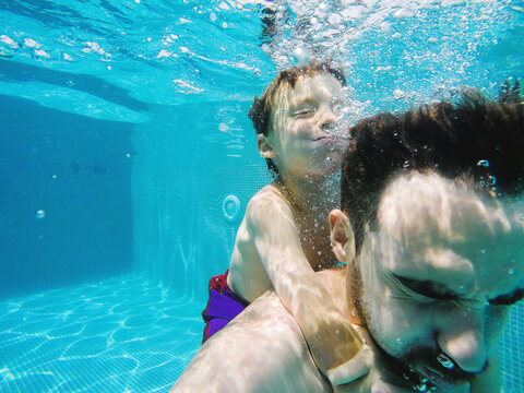 Man and boy holding the breath underwater on the swimming pool.
