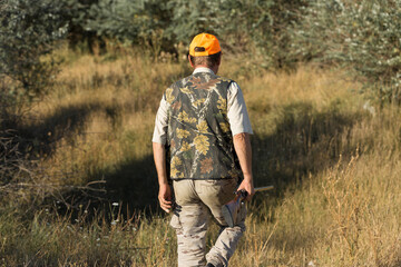 Duck hunter with shotgun walking through a meadow. .Rear view of a man with a weapon in his hands.