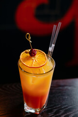 Cocktail with ice and orange liqueur in a tall glass, decorated with cherry and orange.