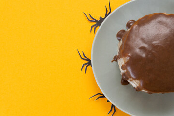 Halloween concept, trick or treat. Spiders from paper crawl out from under a plate. Chocolate cake lies on the right. Orange background, homemade confectionery. Copy space, flat lay. Selective focus.