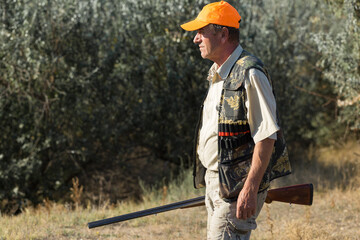 Duck hunter with shotgun walking through a meadow.