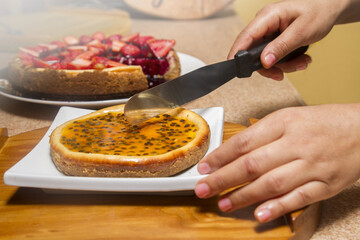 female hands close up with knife cutting cake cheesecake of passion fruit and strawberries at home