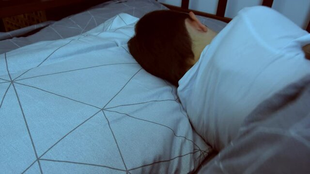 A boy lying in bed at night and turning from one side to the other in order to fall asleep, restless sleep and insomnia concept