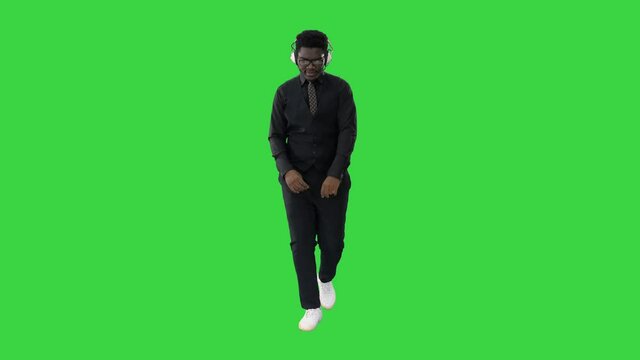 Young african american man listening to music in headphones and grooving while walking on a Green Screen, Chroma Key.