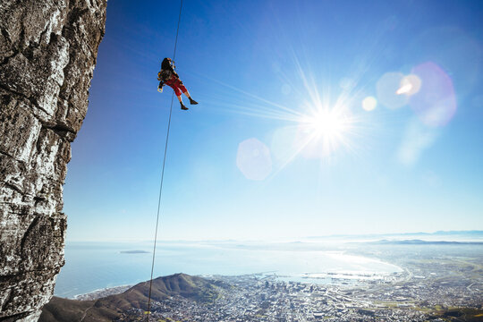 mountaineer abseiling next to a sheer cliff overlooking a city