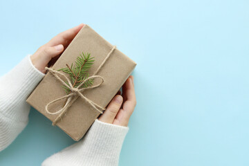 Box with new year's or Christmas present and is decorated in eco style with a sprig of spruce in the women's cacasian hands on a blue background. Copy space