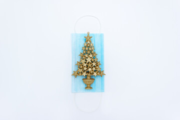 Decorative Christmas tree lies on blue medical mask. Concept of celebrating the New Year during coronavirus epidemic. Flat lay, top view