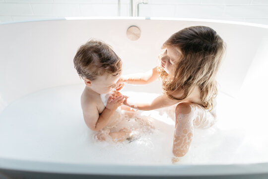Young girl washing her baby brother in a big bathtub