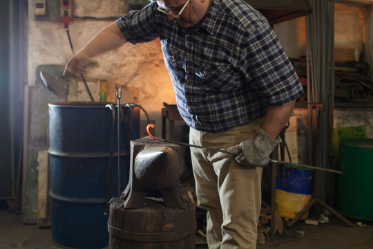 Blacksmith hammering a red-hot artifact in his workshop, Italian craftsmanship.