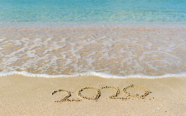 Sea wave next to the inscription 2020 on the beach. The inscription of the ending 2020 in the sand.