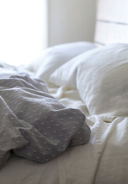 Side of bed with of disheveled pillow, duvet and sheets in natural tones