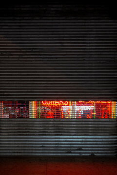 Neon leaks through a security shutter at guitar store