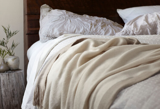 Half of a bed with beige linens with a wood stump night stand