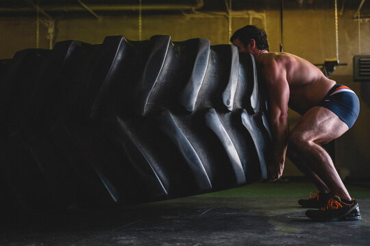 A strong man lifts a large tractor tire in a gym