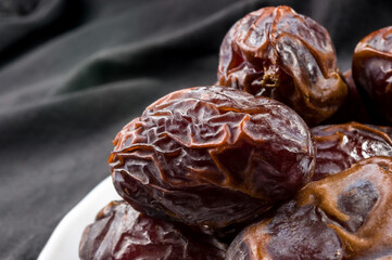 Big luxury dried date fruit in bowls on the dark surface, kurma ramadan kareem concept, close up.