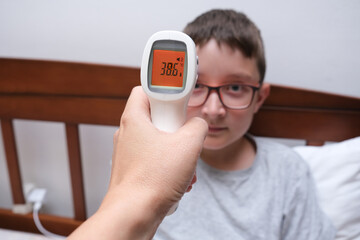 Non-contact infrared thermometer showing high body temperature, unheakthy chuld concept. Mother measuring her son child schoolboy temp at home to make decision about going to school