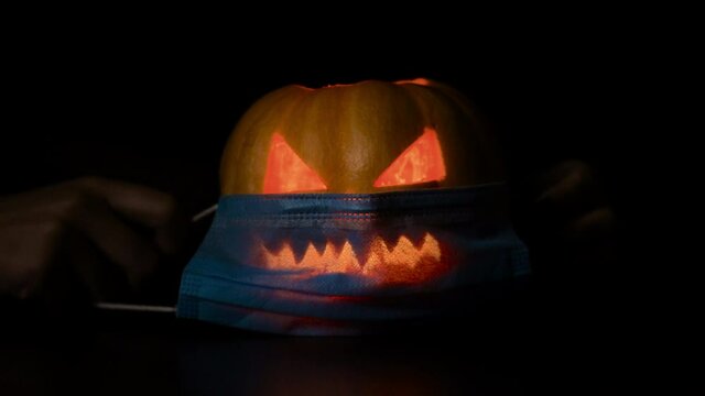 A young woman puts on a protective mask from the virus on a pumpkin at Halloween. Isolated black background.